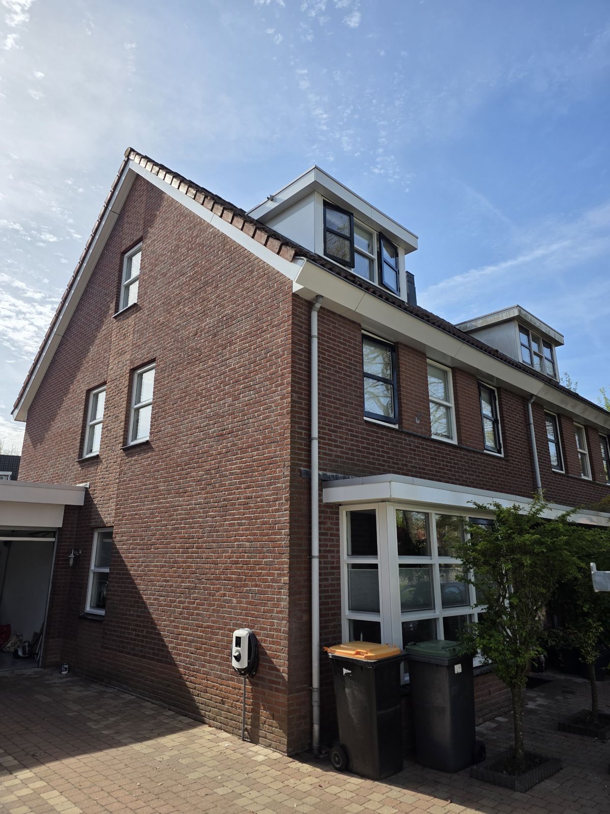 Hoog bakstenen hoekhuis met twee dakkapellen, witte kozijnen en wit schilderwerk