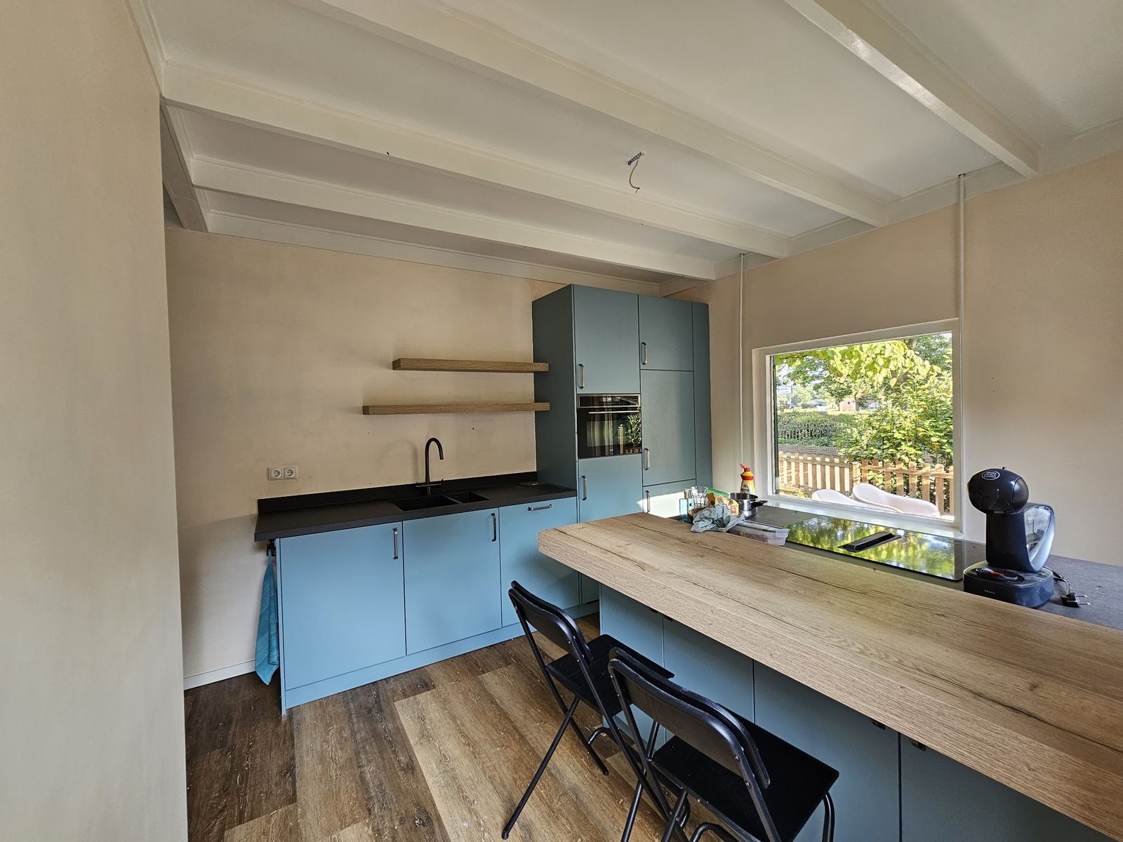 Keuken met blauwe kastjes, houten werkblad en wit balkenplafond