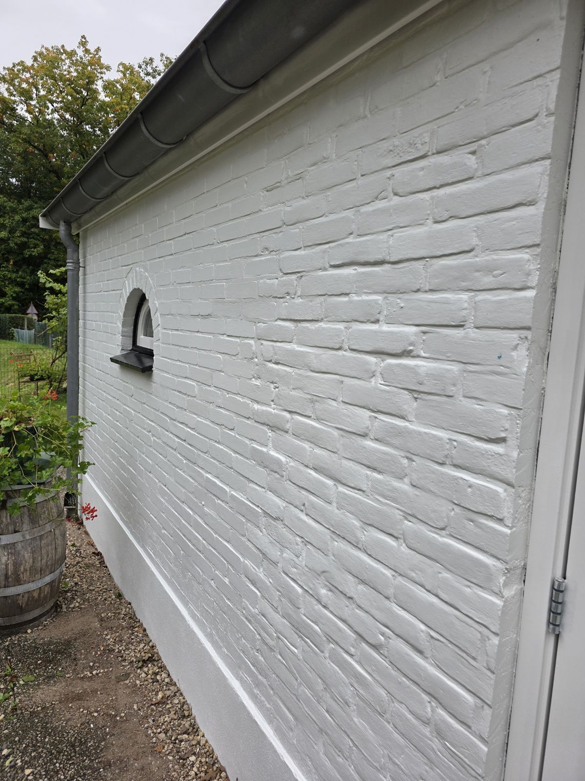 Wit geschilderde bakstenen zijgevel met dakgoot en tuinpad