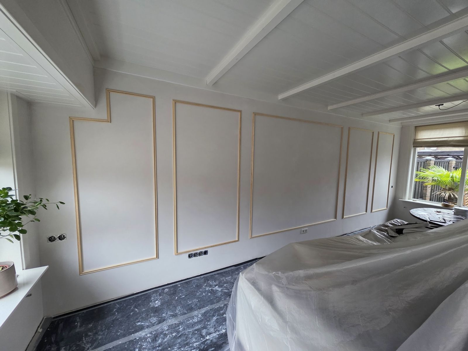 Kamer in uitvoering met witte wanden en sierlijsten, meubels onder plastic