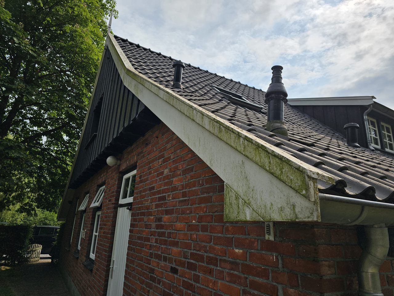 Bakstenen topgevel met verweerd, groen uitgeslagen wit houtwerk en oude dakpannen
